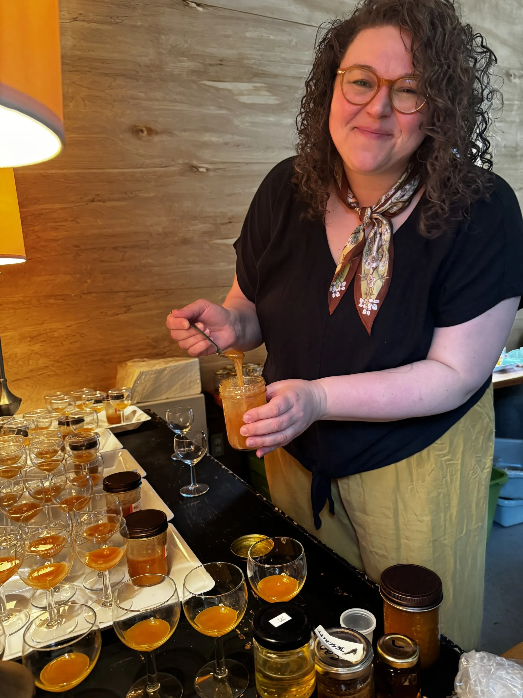 A honey sommelier pouring honey into a tasting glass beside a tray of prepared samples
